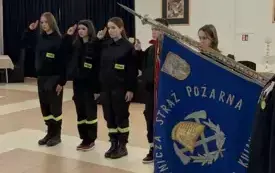 Na pierwszym tle sztandar OSP Złotniki Kujawskie. W tle 4 młodych druch&oacute;w stoi w rzędzie i salutuje