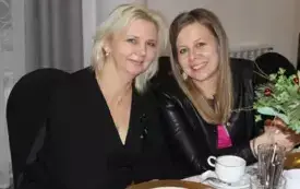 Dwie kobiety siedzą przy stole. Usmiechają się.