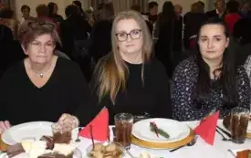 Trzy kobiety siedzą przy świątecznym stole. Na stole biały obrus i zastawa. Kobiety mają zamyslone miny.