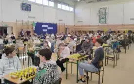 Dzieci siedzą na krzesłach przy stolikach z szachami