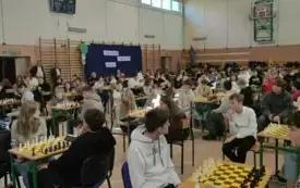 Dzieci siedzą na krzesłach przy stolikach z szachami