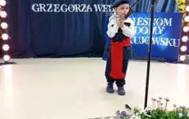 Chłopiec stoi przy mikrofonie ubrany w str&oacute;j ludowy