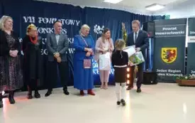 Grupa os&oacute;b stoi, mężczyzna wręcz nagrodę dziecku