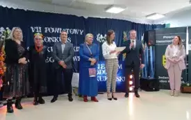 grupa os&oacute;b stoi z nagrodami, mężczyzna przemawia