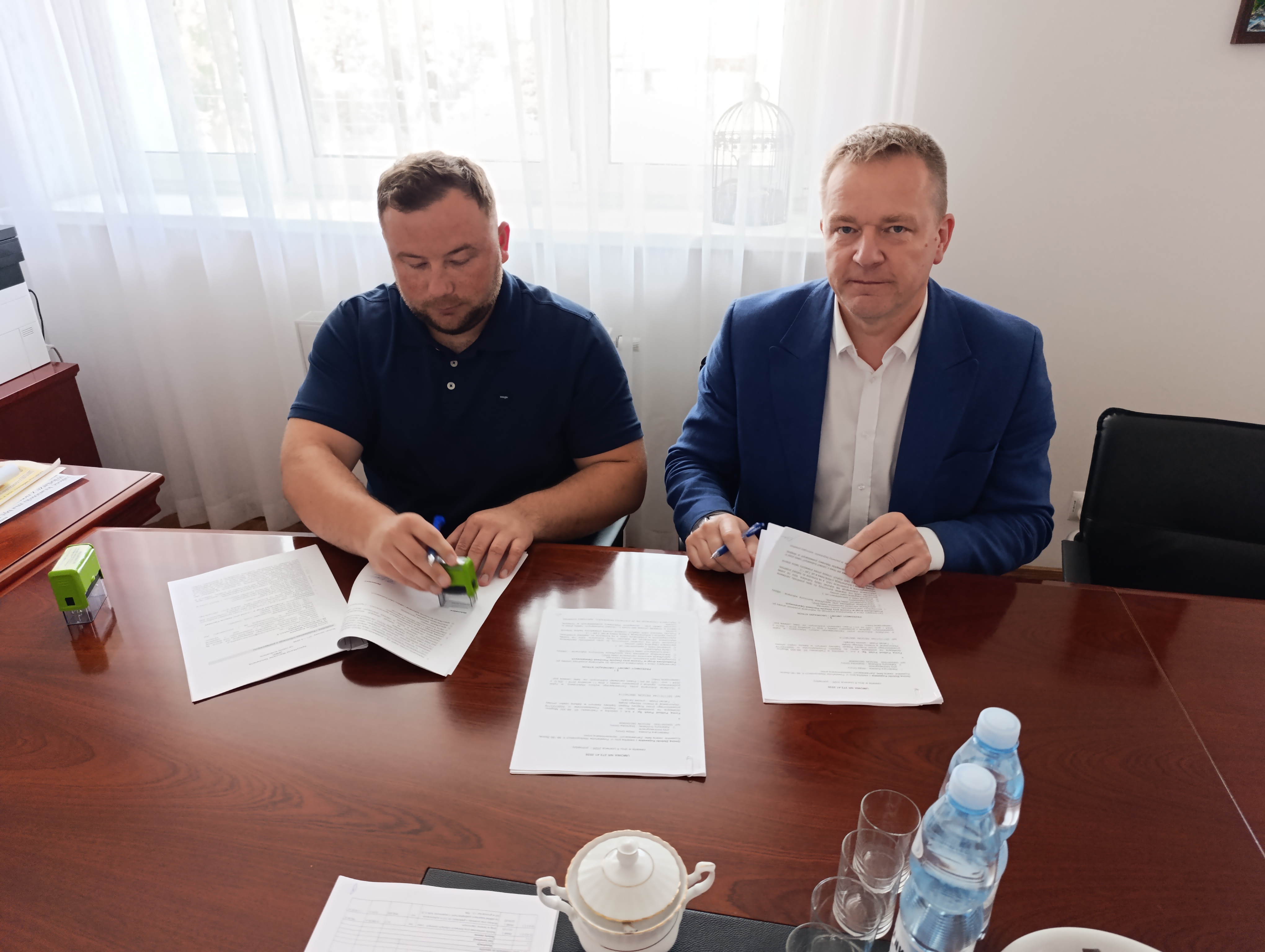 Dw&oacute;ch mężczyzn siedzi i&nbsp;podpisuje dokumenty