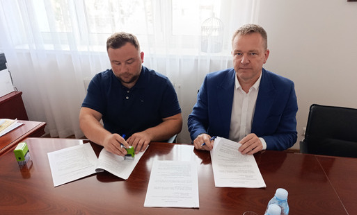 Dwóch mężczyzn siedzi przy stole i podpisuje dokumenty.
